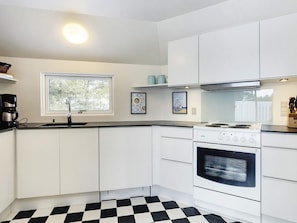 A modern kitchen with white cabinets, a black and white checkered floor, a window, and a stove. - 8 Person Holiday Home in Fjerritslev (Fjerritslev)