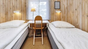 Una habitación con dos camas individuales, un escritorio de madera, una silla, un ventanal con cortinas y lámparas fijadas a la pared.