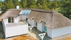 Una casa moderna con techo de paja, un ventanal grande y fachada blanca.