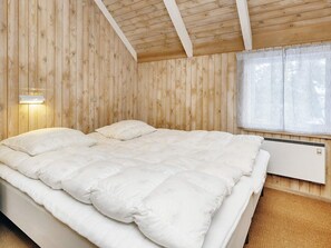 A bedroom with a wooden ceiling, a bed with white bedding, a wall-mounted heater, and a window with blinds. - 8 Person Holiday Home in Fjerritslev (Fjerritslev)