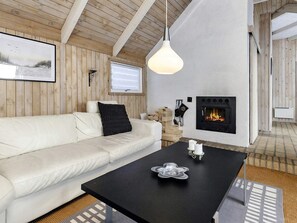 A cozy room with a white sofa, a black coffee table, a fireplace, and wooden walls. - 8 Person Holiday Home in Fjerritslev (Fjerritslev)