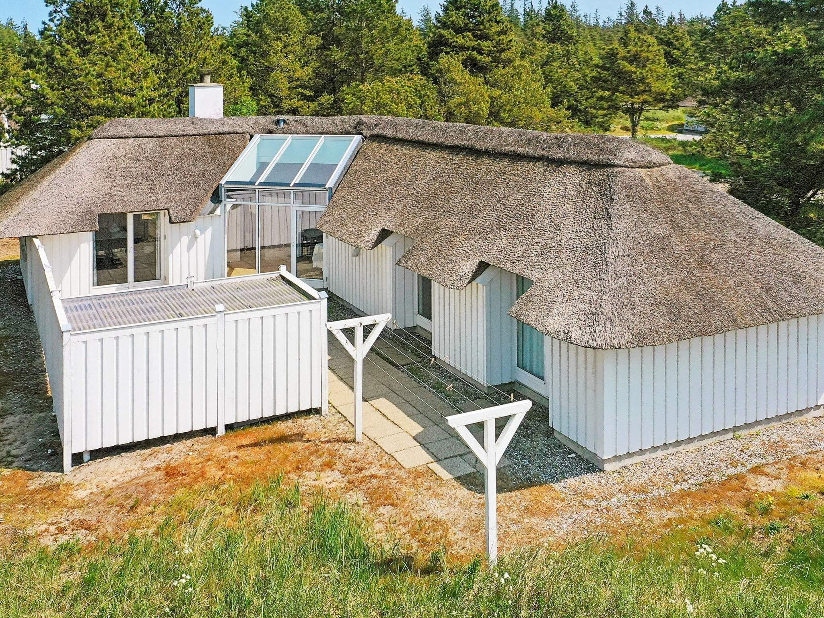 A modern house with a thatched roof, a large window, and a white exterior.