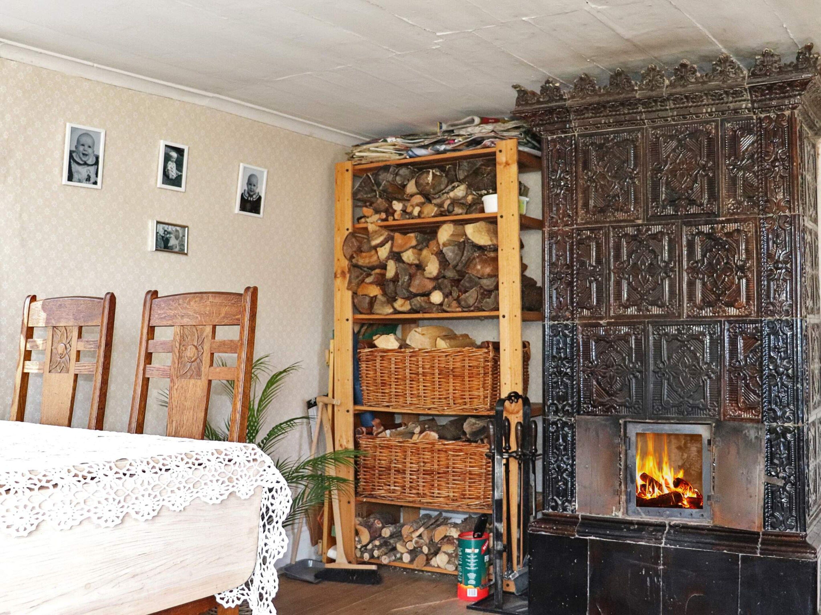 A cozy room with a fireplace, wooden shelves with firewood, a lace tablecloth, and chairs.