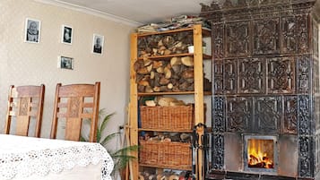 A cozy room with a fireplace, wooden shelves with firewood, a lace tablecloth, and chairs.