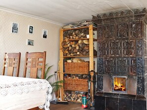 Een gezellige kamer met een open haard, houten planken met houtblokken, een kantkleed en stoelen.