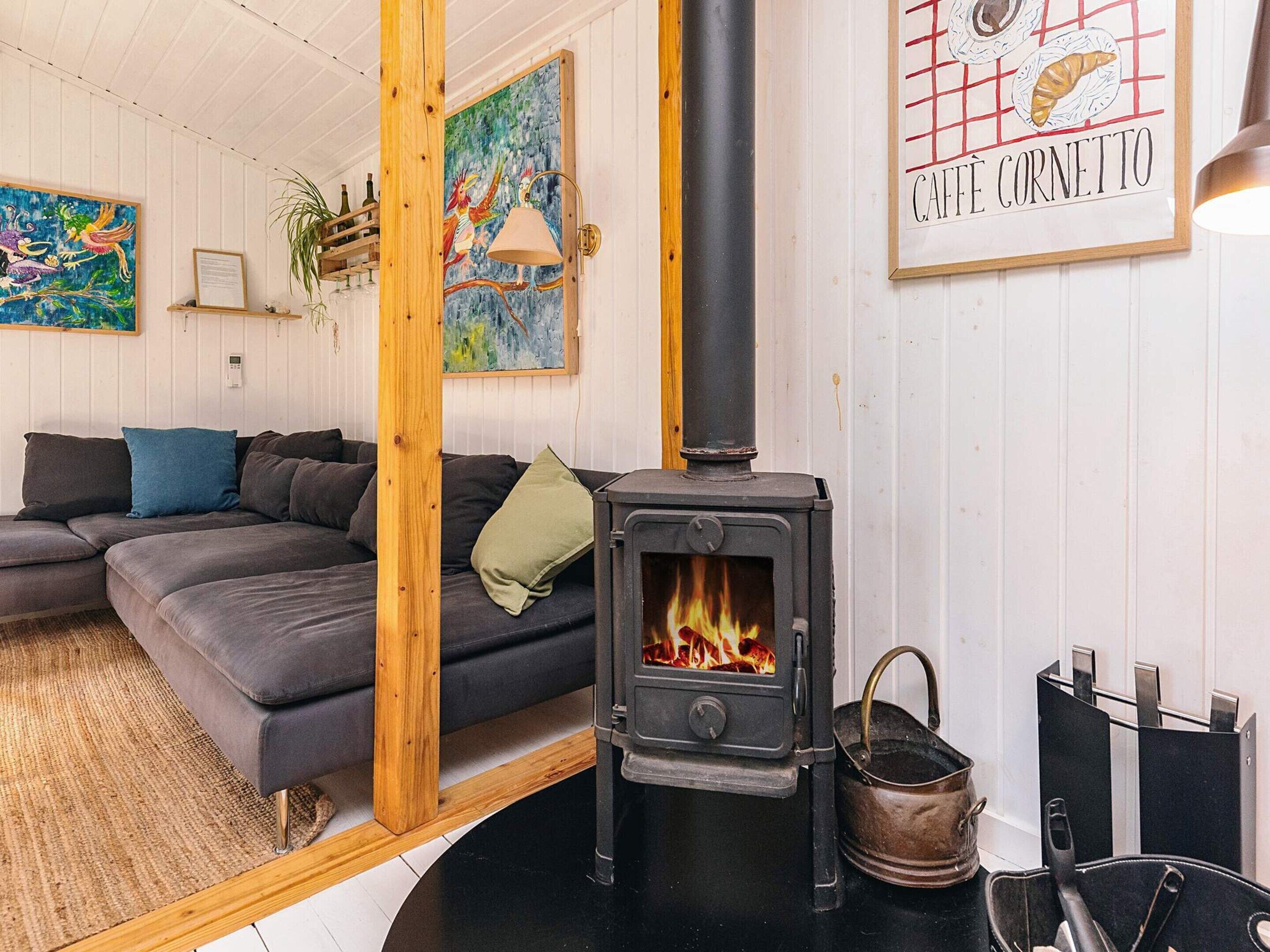 A cozy living room with a modern sofa, a wooden accent wall, a painting, and a black wood-burning stove.