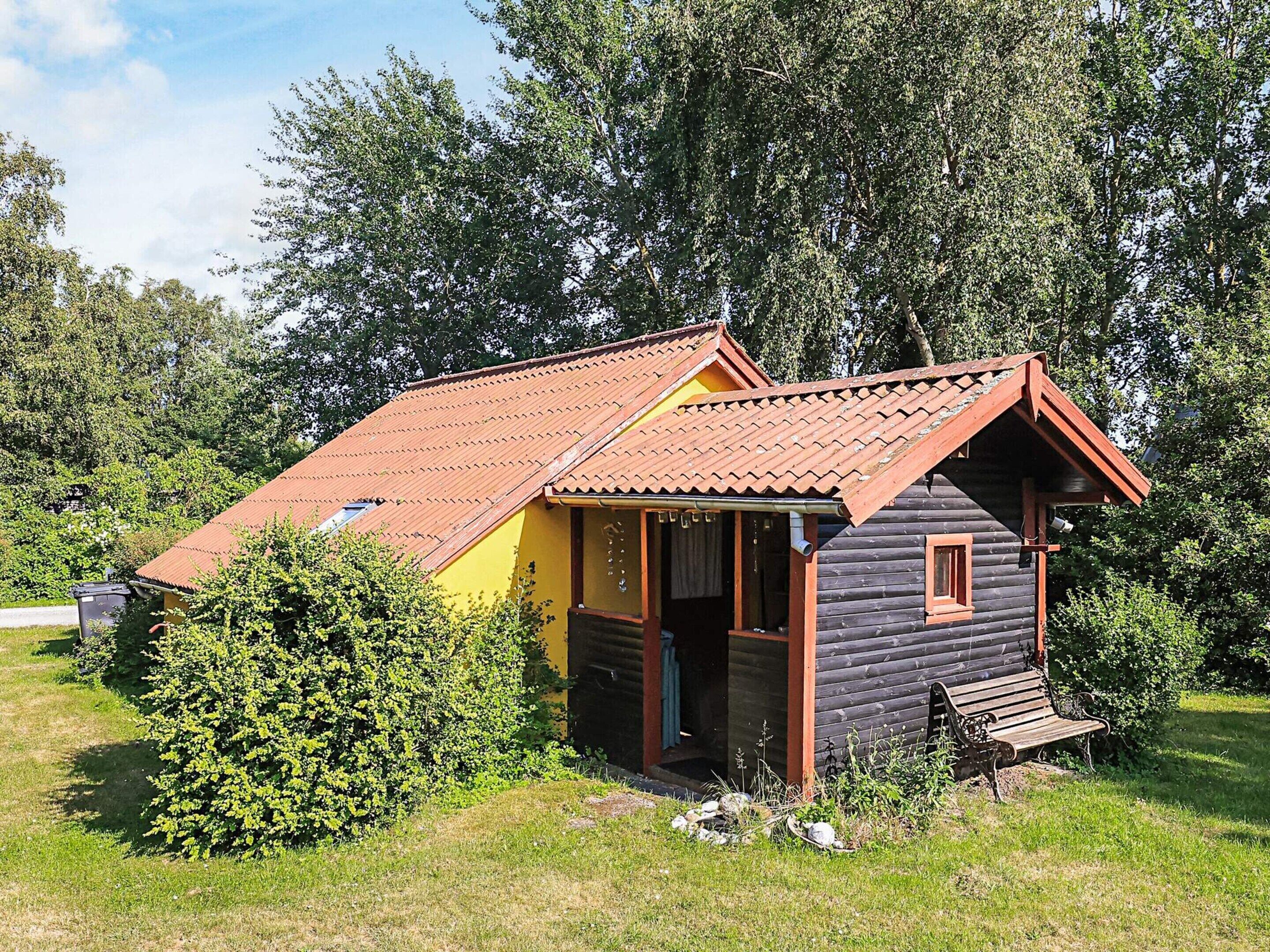 A small wooden cabin with a red roof, surrounded by greenery.