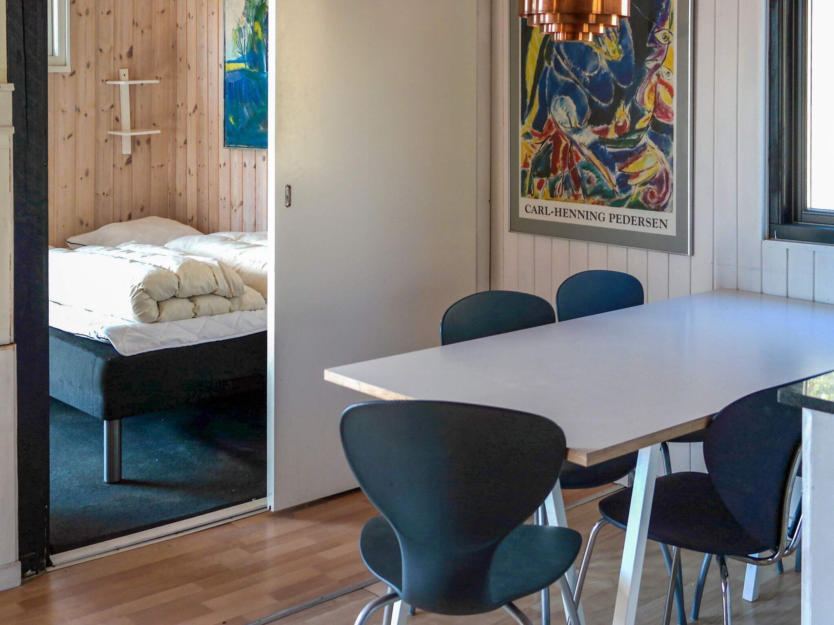 A room with a bed, a table, and chairs. There is a painting on the wall and a window.