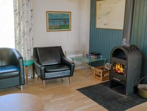 A living room with a black leather armchair, a glass table, a wooden crate, and a wood-burning stove. - 6 Person Holiday Home in Saltum (Saltum)