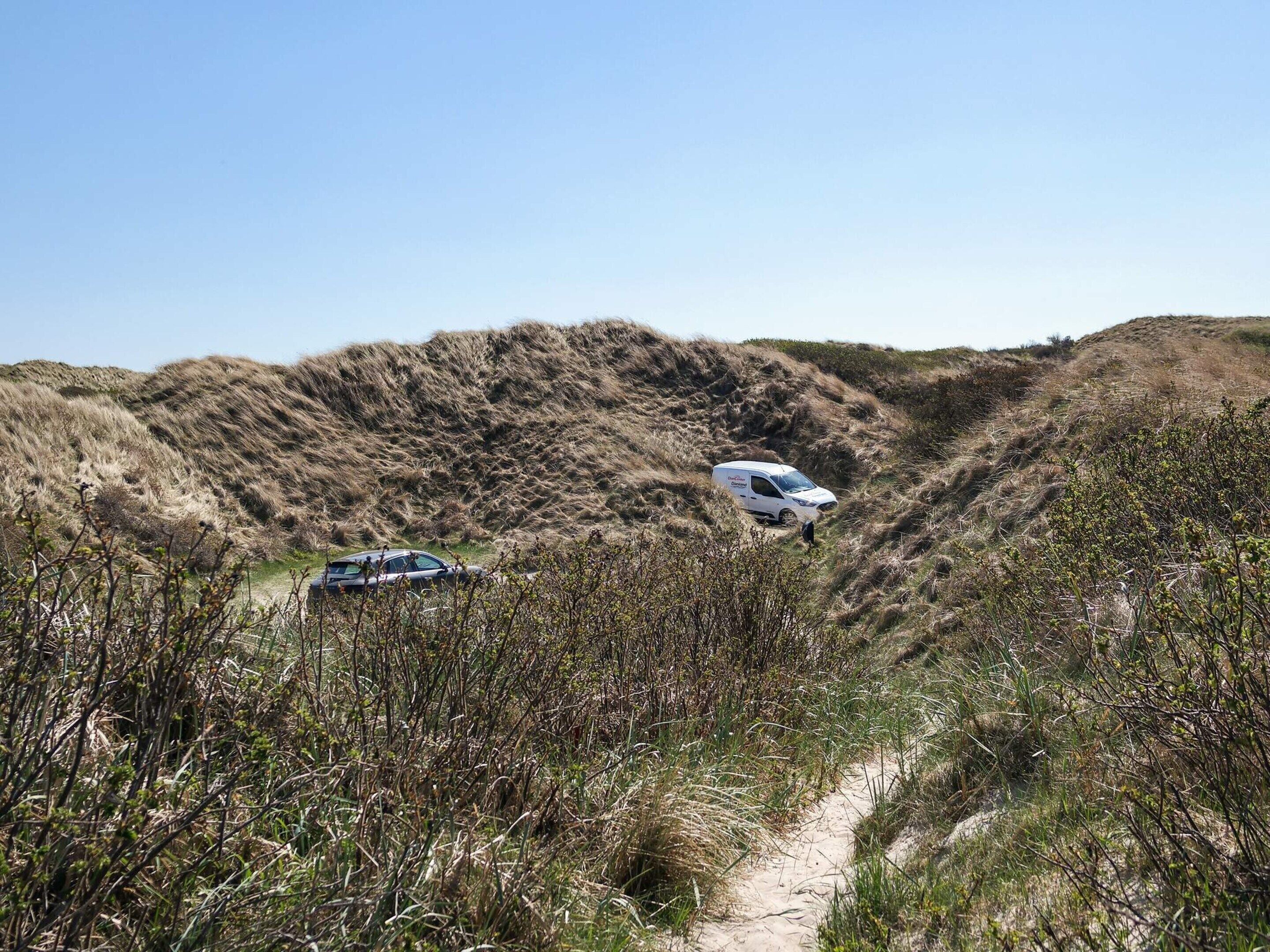 Un fourgon blanc était garé sur un chemin de sable, entouré d’herbes sèches et de buissons.