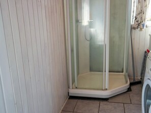 A corner of a room with a shower enclosure, a washing machine, and a tiled floor.
