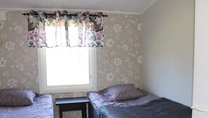 A bedroom with two single beds, a small table, and a window with floral curtains.