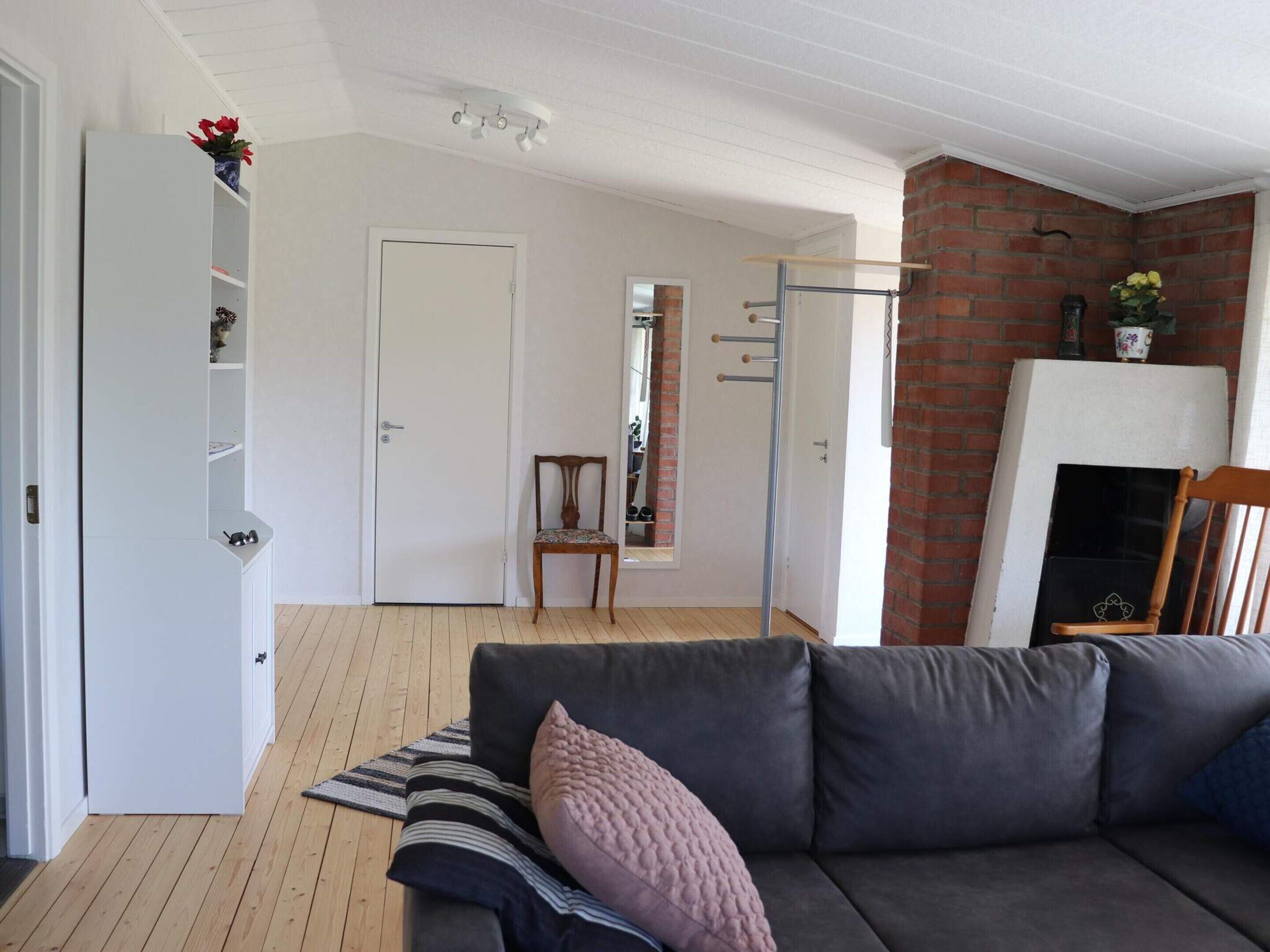 Un salon avec un canapé gris, un plancher en bois, une porte blanche, un mur en briques et une cheminée.