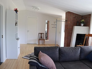 A living room with a grey sofa, a wooden floor, a white door, a brick wall, and a fireplace. - 5 Person Holiday Home in Traslovslage (Träslövsläge)