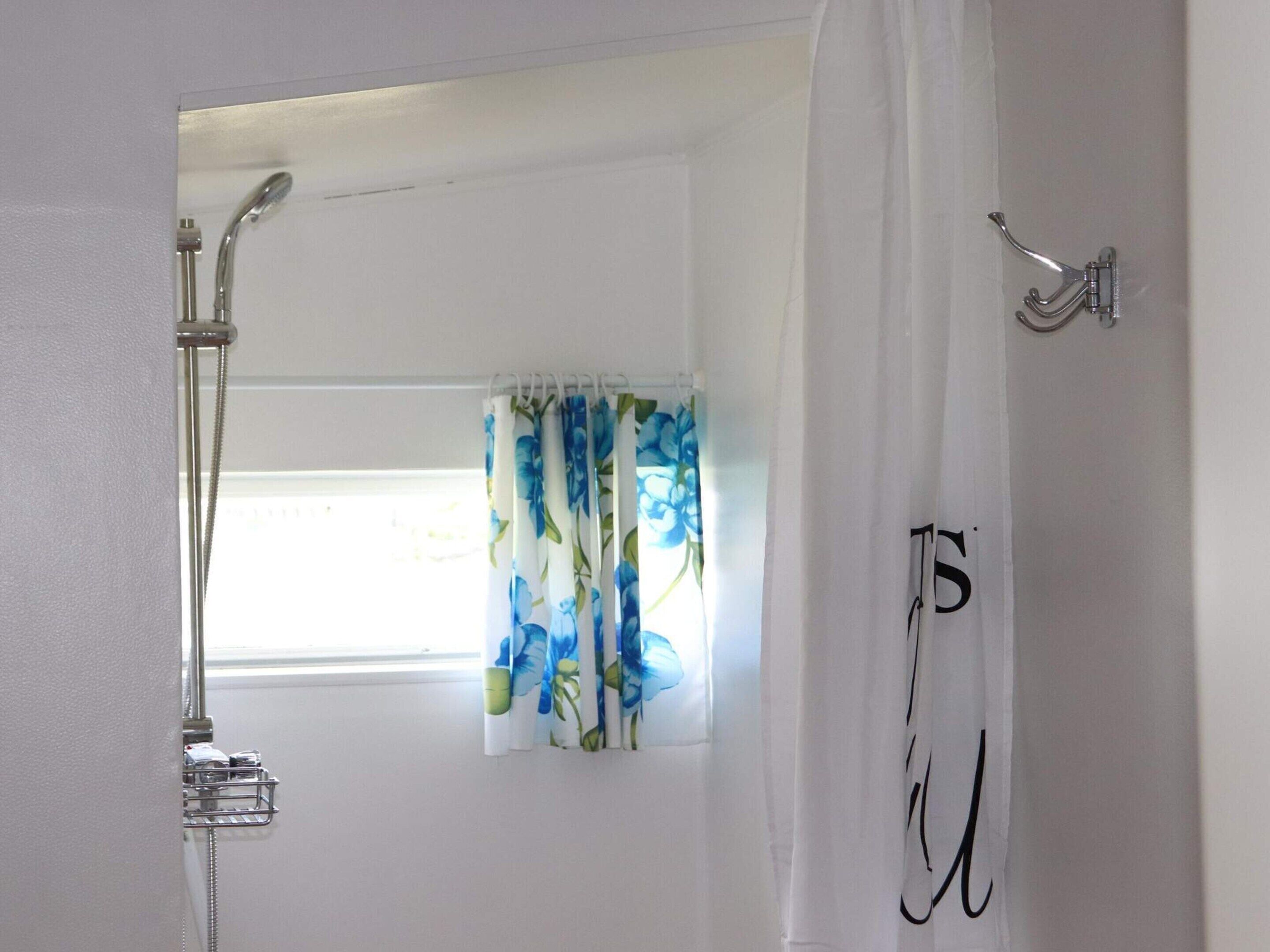 A bathroom with a shower, a window with floral curtains, and a towel rack.