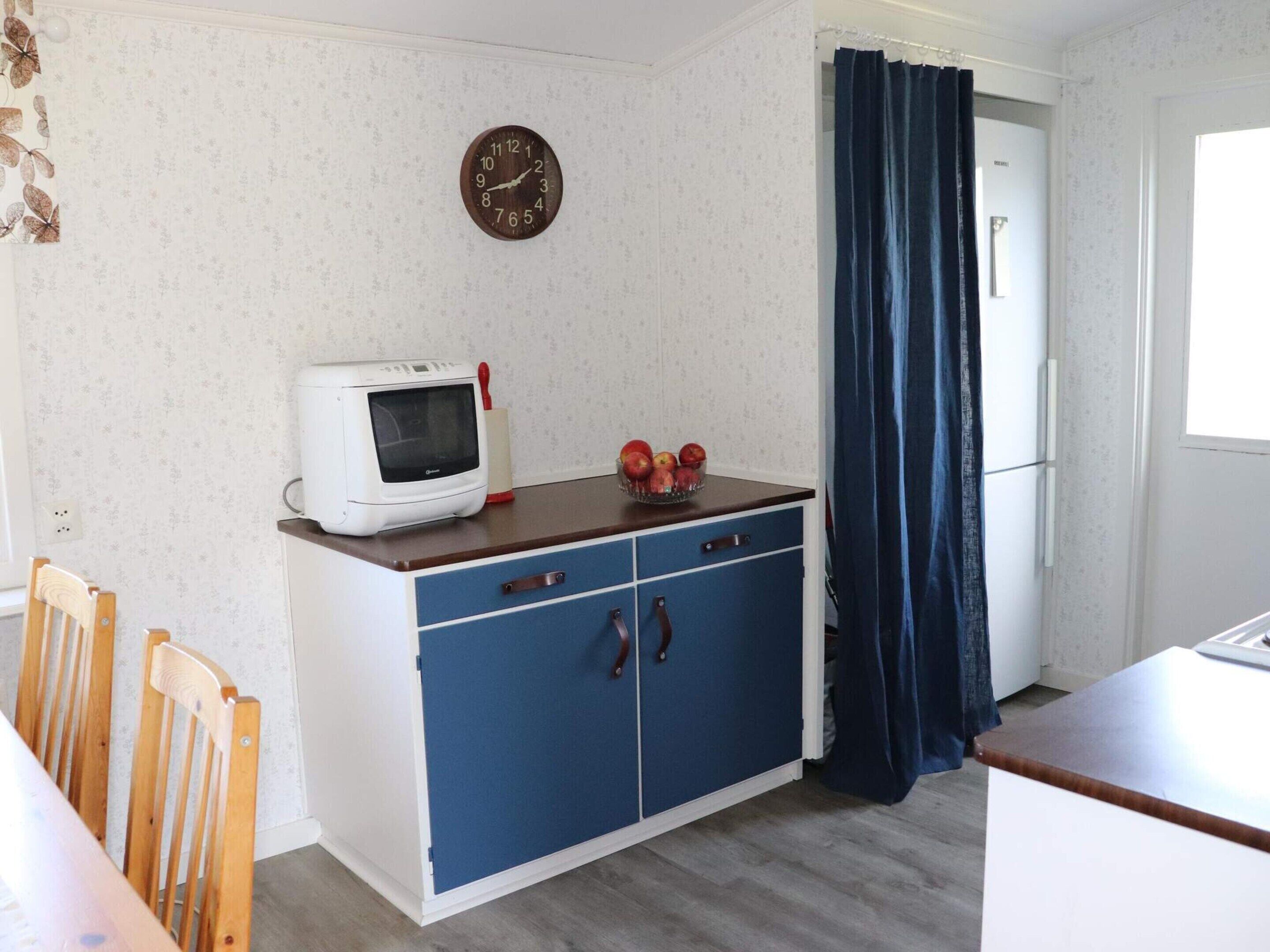 A kitchenette with a microwave, a fruit bowl, and a clock on the wall.