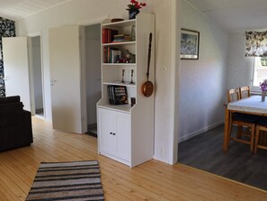 A room with a white bookshelf, a dining table with chairs, and a patterned rug. - 5 Person Holiday Home in Traslovslage (Träslövsläge)