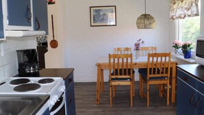 A compact kitchen with a stove, microwave, and coffee maker. There is a dining table with chairs and a window with curtains.
