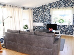 A living room with a grey sofa, a black table with a bowl of fruit, a TV, and a window with a wreath. - 5 Person Holiday Home in Traslovslage (Träslövsläge)