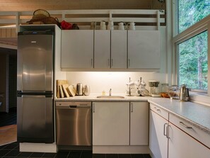 A modern kitchen with stainless steel appliances, white cabinetry, and a window with a view of trees. - 4 Star Holiday Home in Vejby (Vejby)