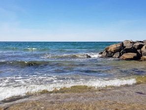A beach with clear water, rocks, and a clear sky.