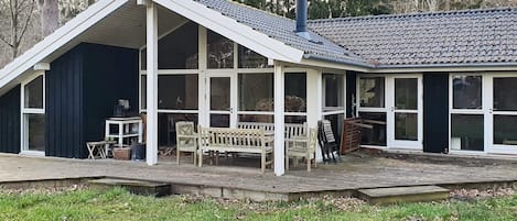 A house with a sloped roof, large windows, and a porch with a bench.