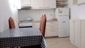 A small kitchen with white cabinets, a stove, a refrigerator, and a television on top. - Apartment Mijatovic - One Bedroom Apartment with Terrace (Vodice)