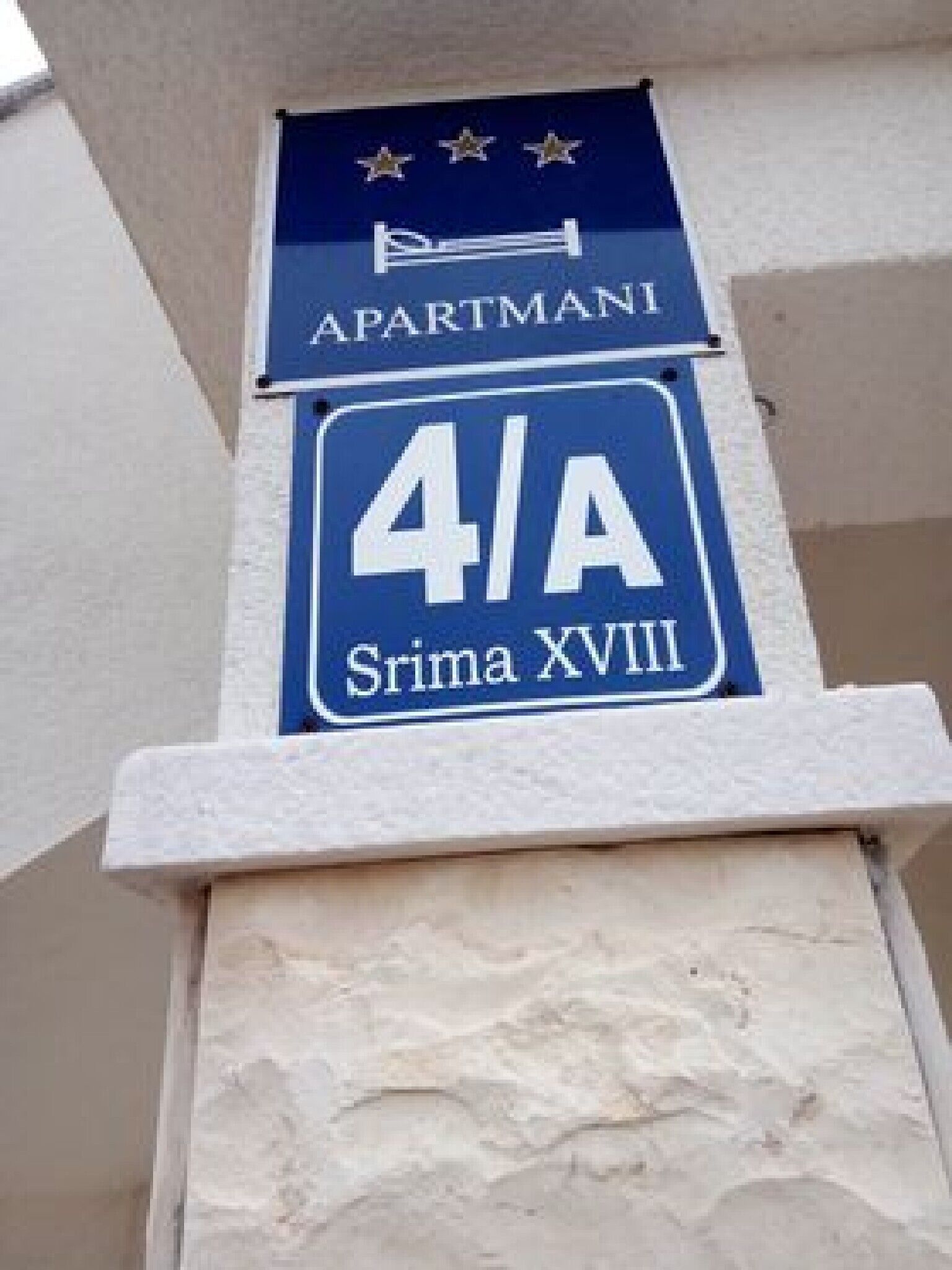 Schild mit 'APARTMANI 4/A' und darunter 'Srima XVIII', befestigt an einem Steinsäule.