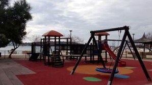 A playground with a swing set and a climbing structure, surrounded by a red carpet and a tiled area. - Apartment Mijatovic - One Bedroom Apartment with Terrace (Vodice)