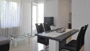 A modern dining area with a glass table, black chairs, and a television in the background. - Apartments Profaca - Two Bedroom Apartment with Terrace (Rab)