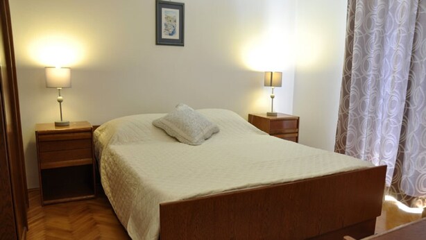 A bedroom with a wooden bed, two bedside tables with lamps, a framed picture on the wall, and a patterned rug on the floor. - Apartments Profaca - Two Bedroom Apartment with Terrace (Rab)