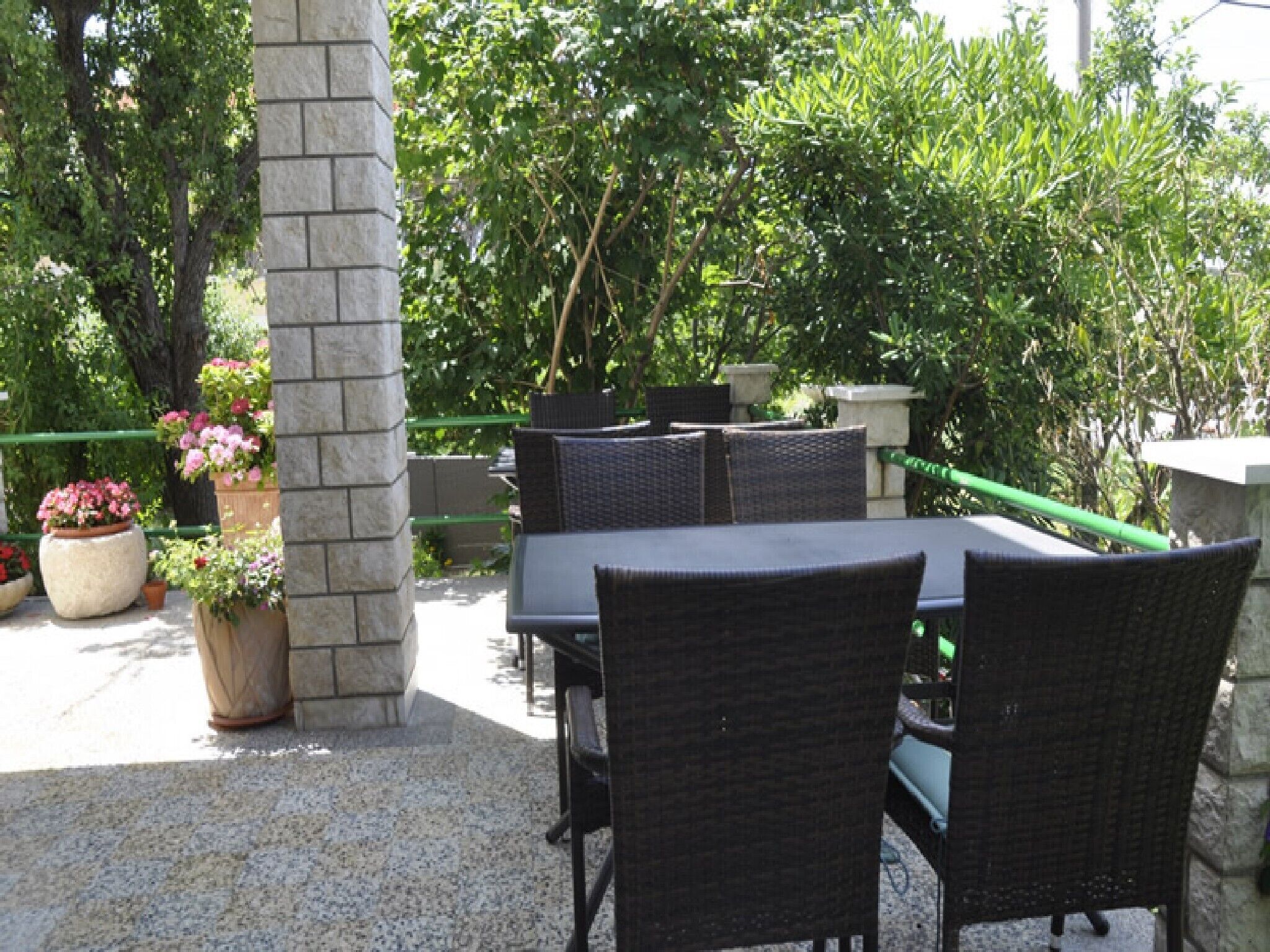 Un patio al aire libre con un pilar de piedra, mobiliario de mimbre y plantas en macetas.