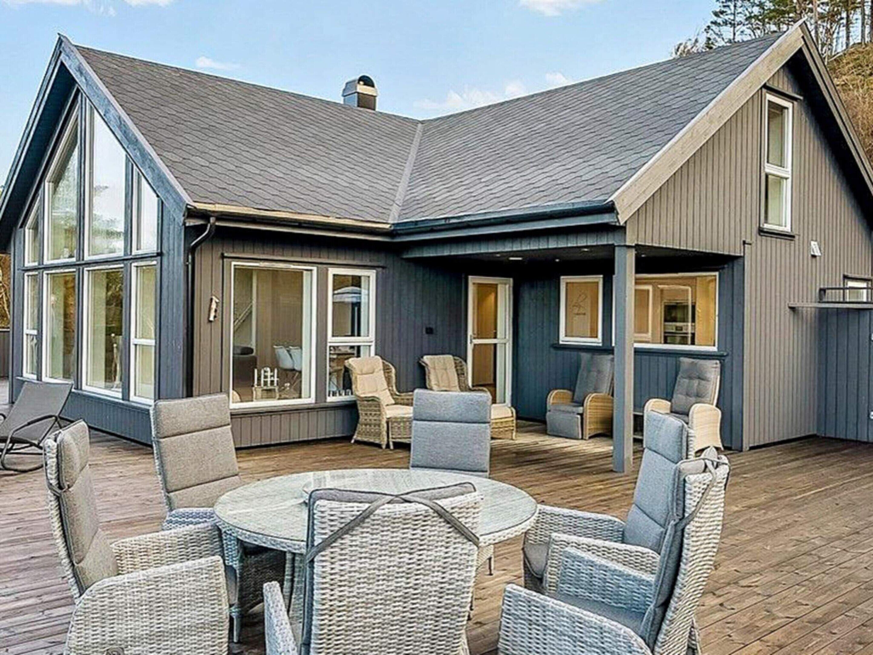 A modern house with a large deck, outdoor seating area, and large windows.