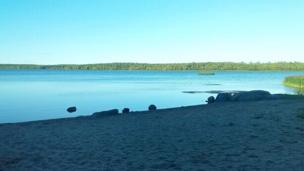 A calm lake with a sandy beach and scattered rocks. - 5 Person Holiday Home in Lulea-by Traum (Luleå)