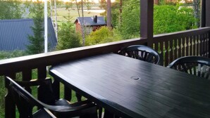 A covered outdoor area with a table and chairs, overlooking a grassy area and a building with a red roof. - 5 Person Holiday Home in Lulea-by Traum (Luleå)