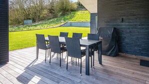 An outdoor patio with a table and chairs, a grill, and a view of a grassy area and trees.
