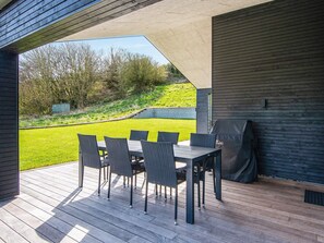Un patio exterior con mesa y sillas, una parrilla y vistas a un área verde y árboles.