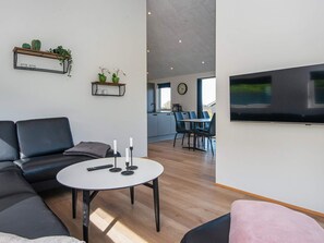 Ein modernes Wohnzimmer mit einer Couch, einem runden Couchtisch mit Kerzen und einem flachbildfernseher an der Wand.