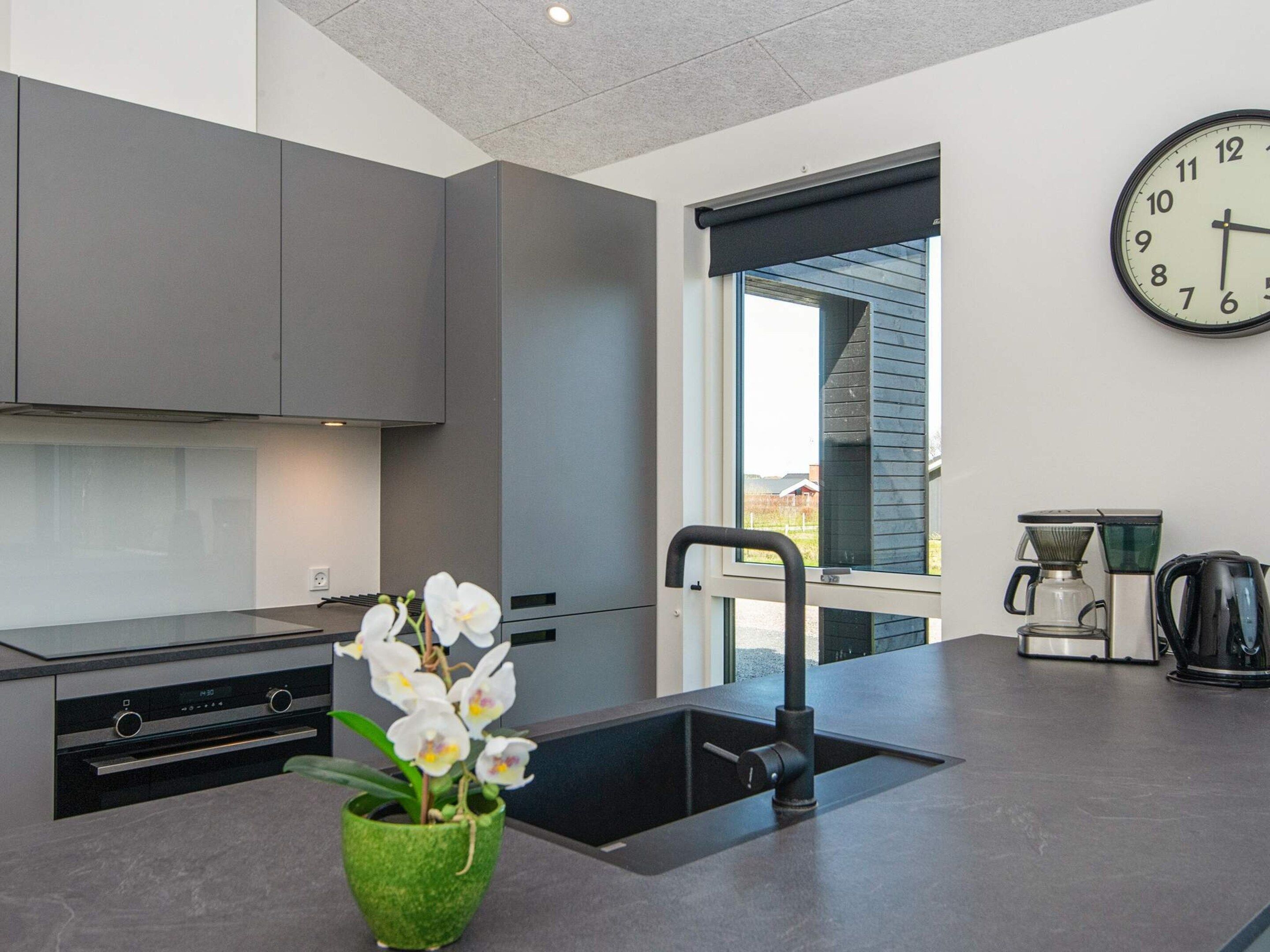 A modern kitchen with a built-in oven, a sink, and a clock on the wall.