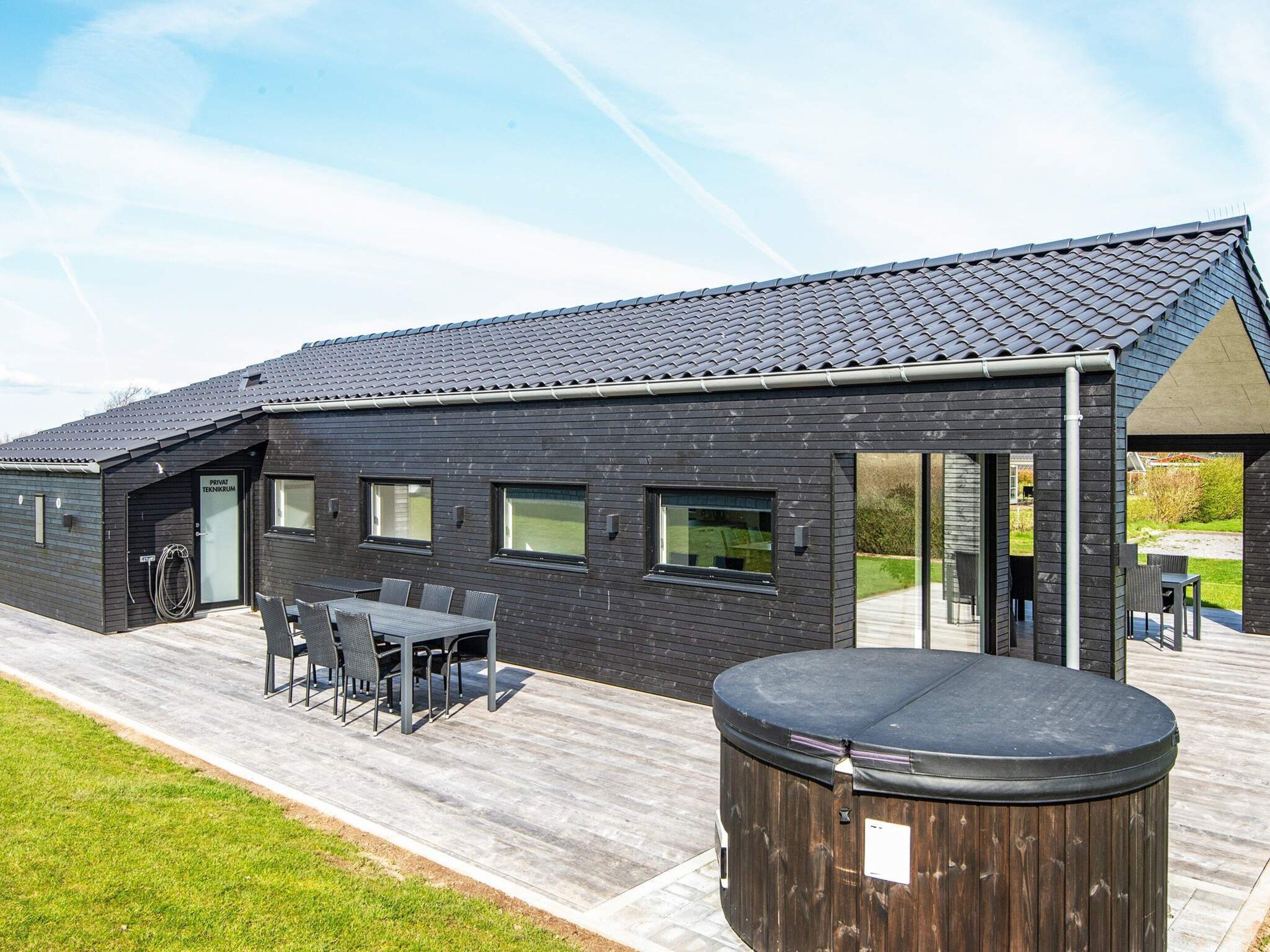 A modern building with a dark exterior, a covered patio area with outdoor seating, and a hot tub.