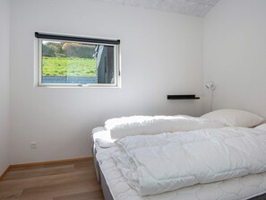 A bedroom with a bed, a window, a wall-mounted shelf, and a power outlet.