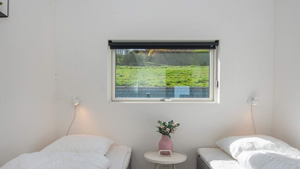 A bedroom with two beds, a small table with a vase, and a window with a view of greenery.