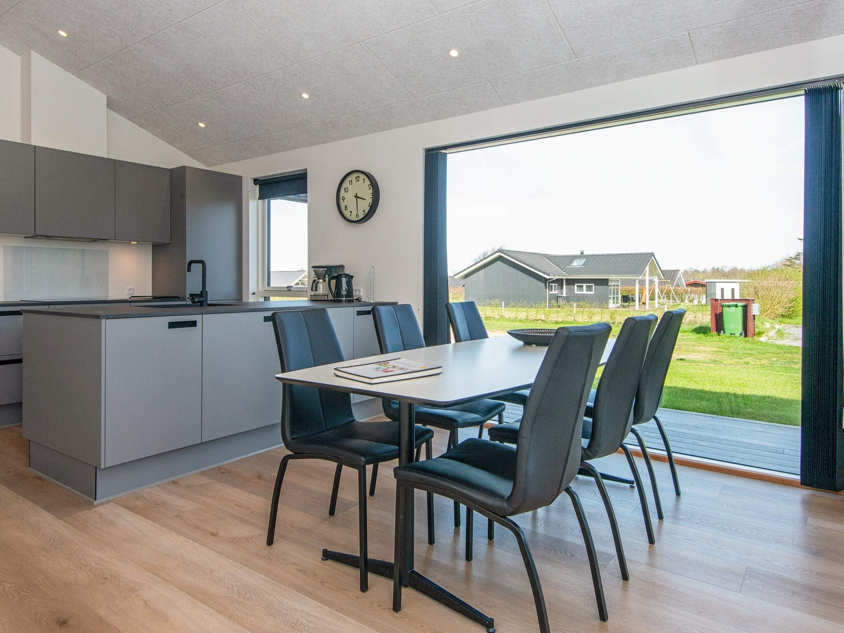 A modern kitchen with a dining area, a clock on the wall, and a view of the outside.