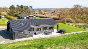 A modern building with a flat roof, a patio area with outdoor seating, and a view of the surrounding landscape.