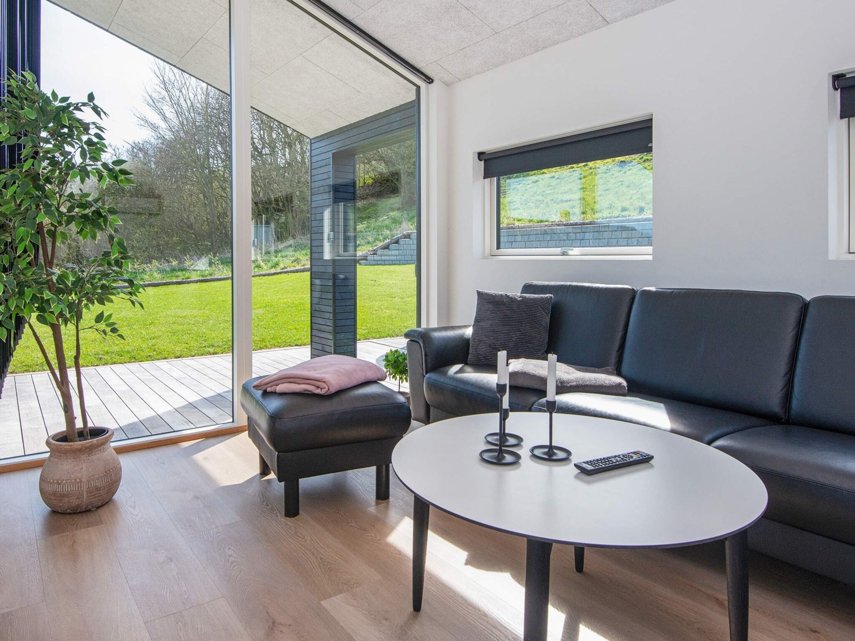 A modern living room with a glass door leading to a balcony, a black leather sofa, a round coffee table, and a potted plant.