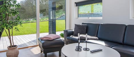 A modern living room with a glass door leading to a balcony, a black leather sofa, a round coffee table, and a potted plant.