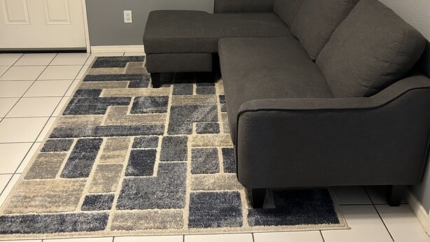Una sala de estar con un sofá modular gris, un tapete estampado y dos cuadros colgados en la pared.