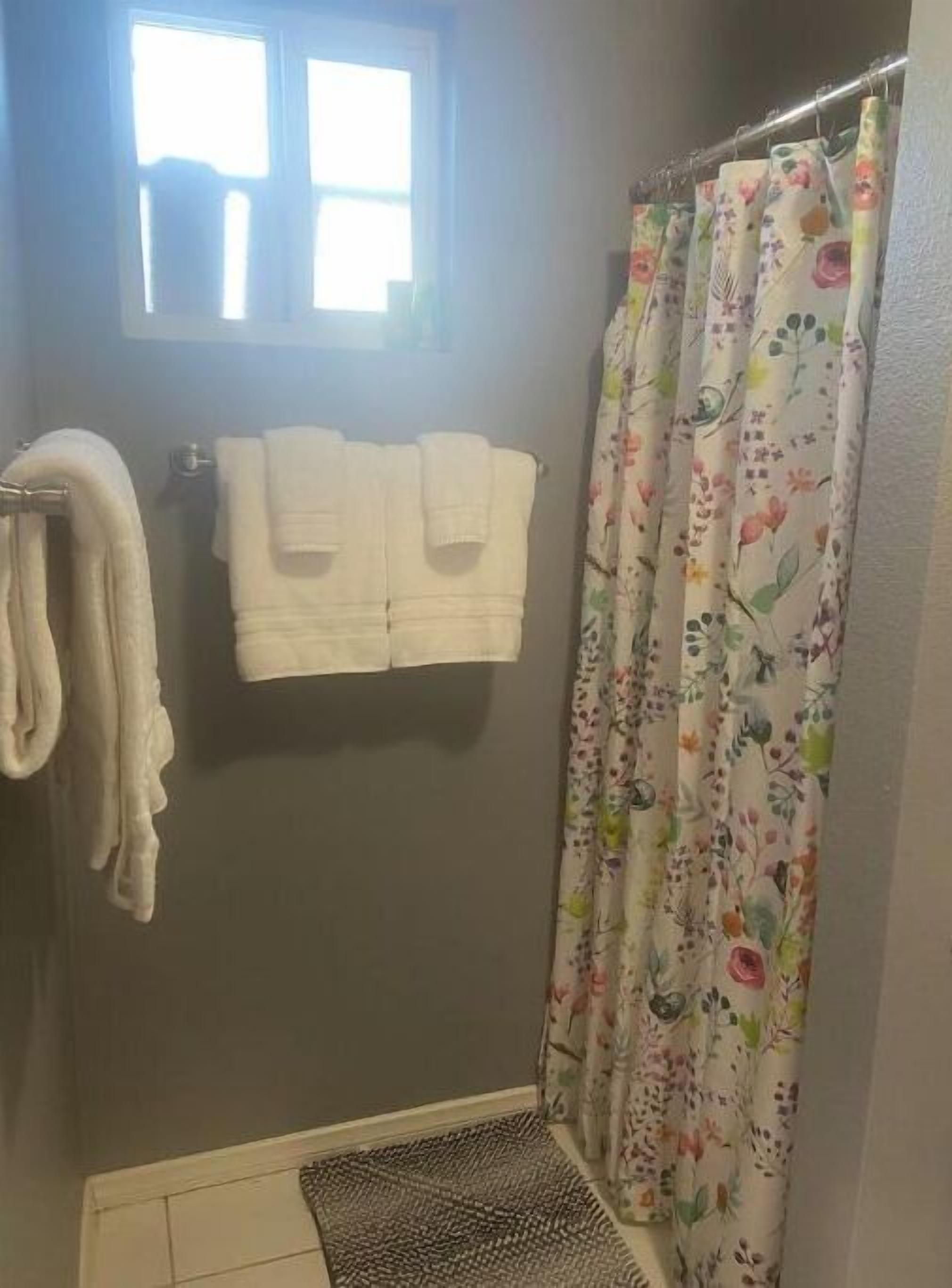 Une salle de bain avec un rideau de douche, deux serviettes blanches et une petite fenêtre.