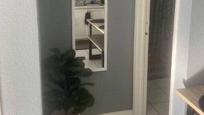 Un pasillo estrecho con un espejo de marco blanco, una planta en maceta y piso de baldosas.