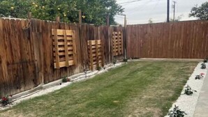 Un patio trasero con cerco de madera, césped y un sendero de grava con flores rojas.